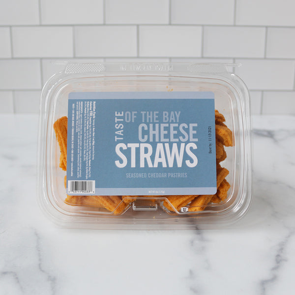 A resealable plastic container of TASTE of the Bay Cheese Straws on a marble surface.