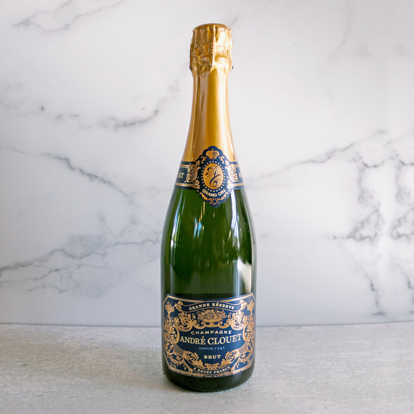 A bottle of Andre Clouet, Champagne Brut with a golden foil top and a blue and gold label on a marble background.
