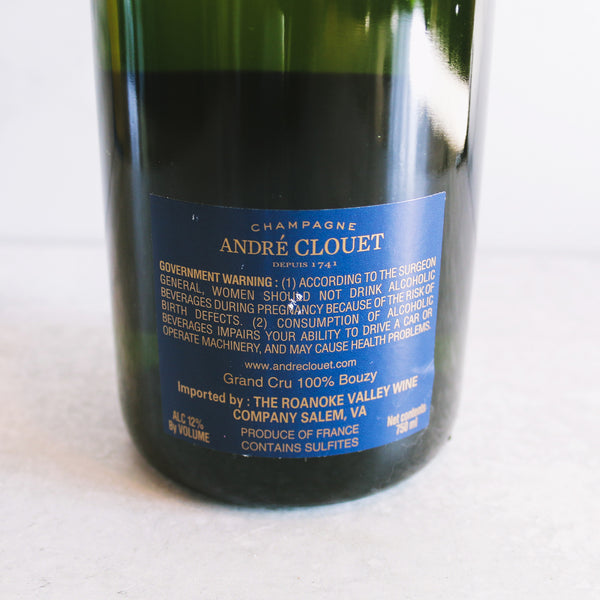 A bottle of Andre Clouet, Champagne Brut with a golden foil top and a blue and gold label on a marble background.