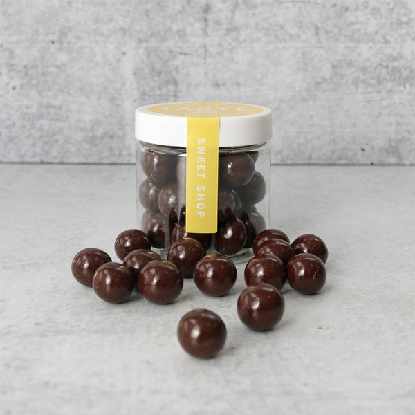 A clear jar of dark chocolate sea salt caramels from TASTE Sweet Shop on a grey surface, with some candies spilling out in front of the jar.