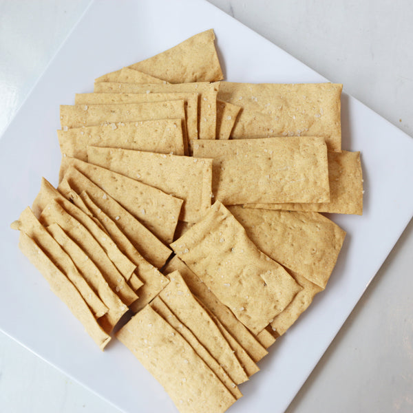 A plate of rectangular, light brown sea salt crackers arranged on a white plate.