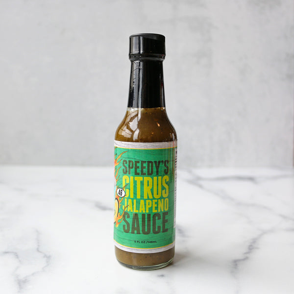 A bottle of Speedy's Citrus Jalapeno Hot Sauce on a marble surface.
