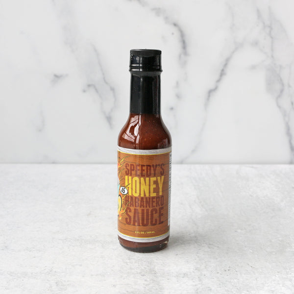 A bottle of Speedy's Honey Habanero Hot Sauce on a marble surface.