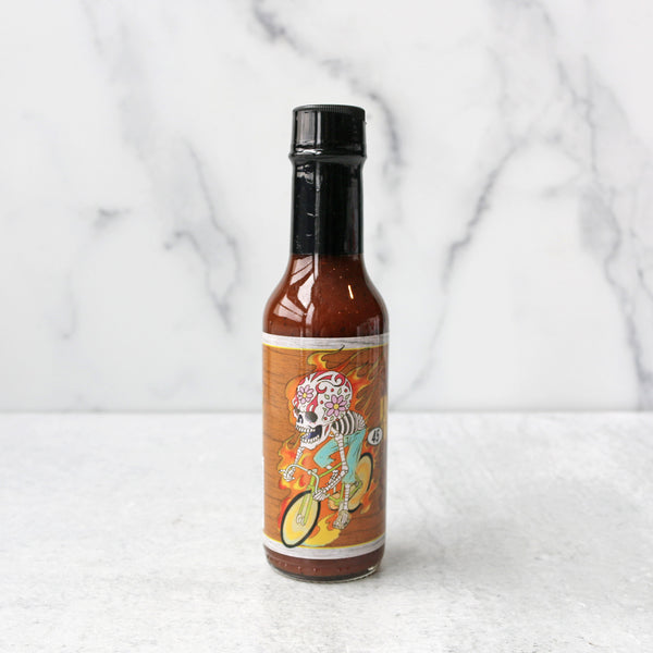 A bottle of Speedy's Honey Habanero Hot Sauce on a marble surface.