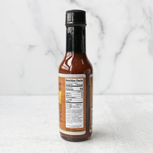 A bottle of Speedy's Honey Habanero Hot Sauce on a marble surface showing nutrition facts