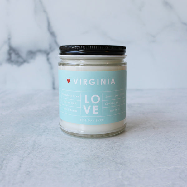 A jar candle with a white label that reads 'VIRGINIA LOVE' on a blue and green striped background, placed on a marble surface.